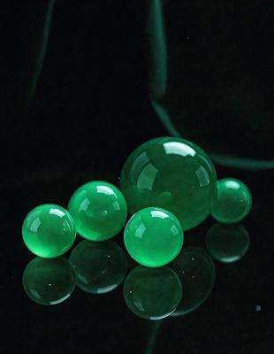 The primary subject of the image is a group of four green glass balls. They are placed on a black surface, which serves as the setting or background. The visual style of the image is a photo, capturing the details and colors of the glass balls. The dominant colors in the image are green, which gives the scene a lively and vibrant atmosphere.